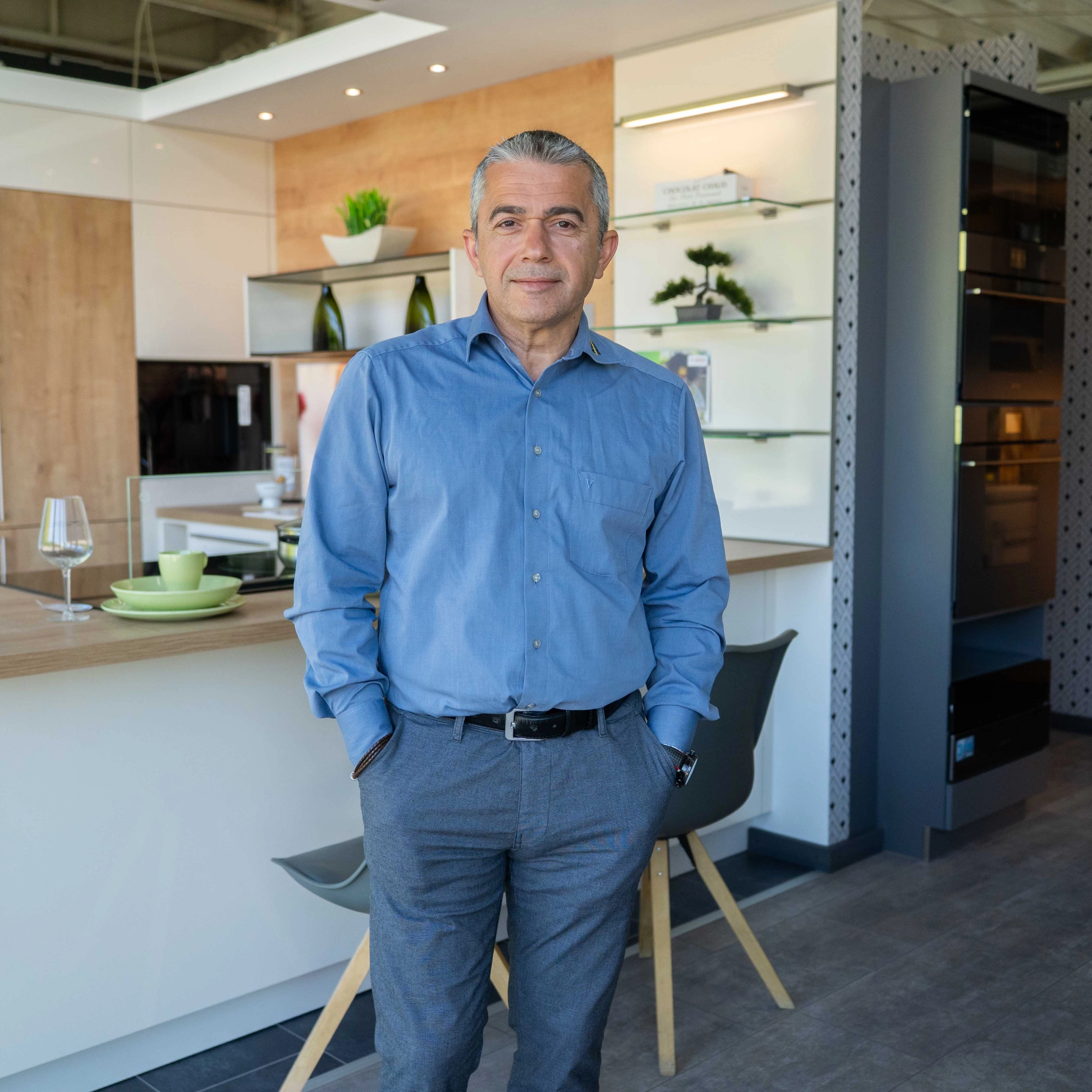 Un homme se tient dans une cuisine moderne aux tons bois et blanc. Nolte Kitchen.