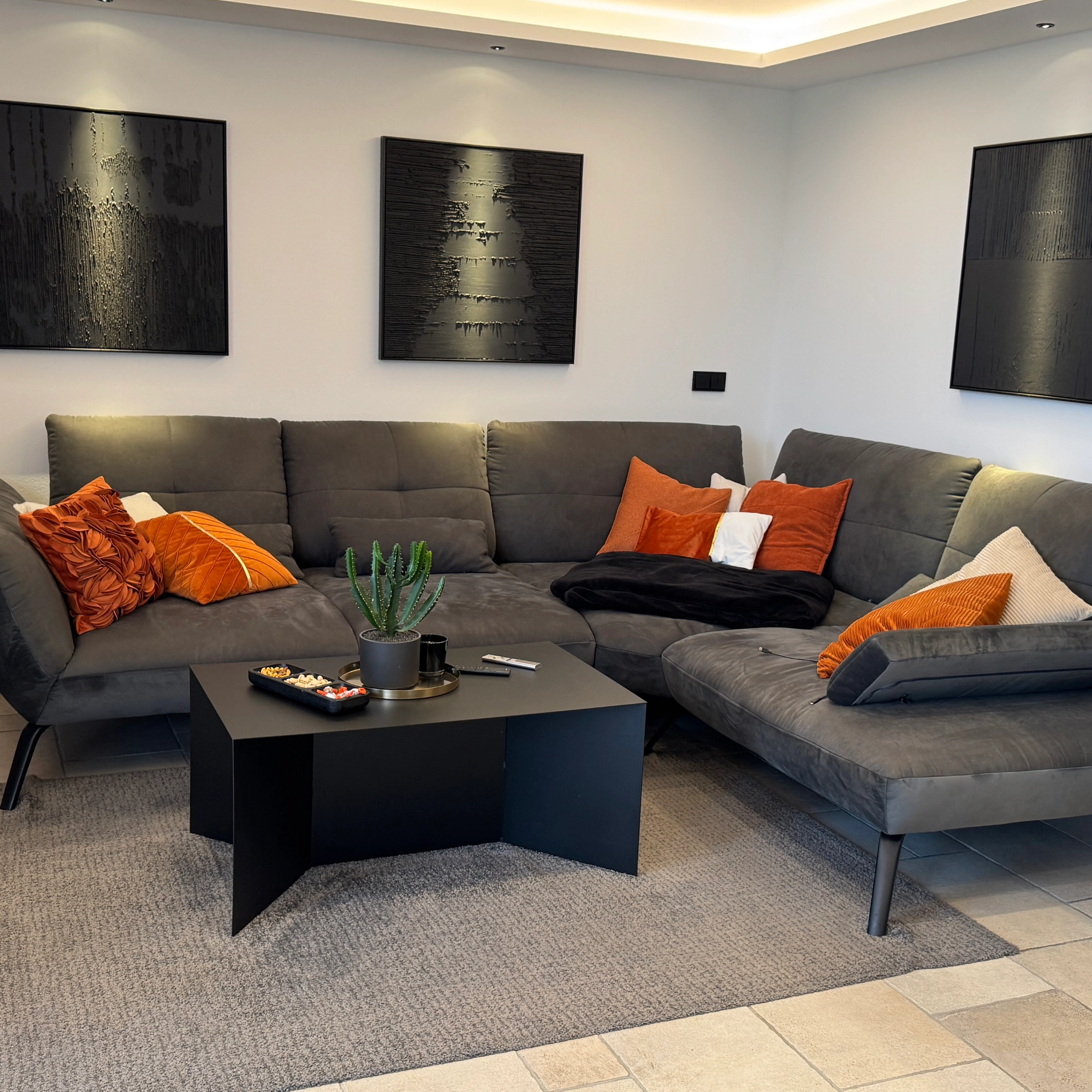 Soggiorno moderno con divano grigio e cuscini arancioni, arricchito da Nolte Living.