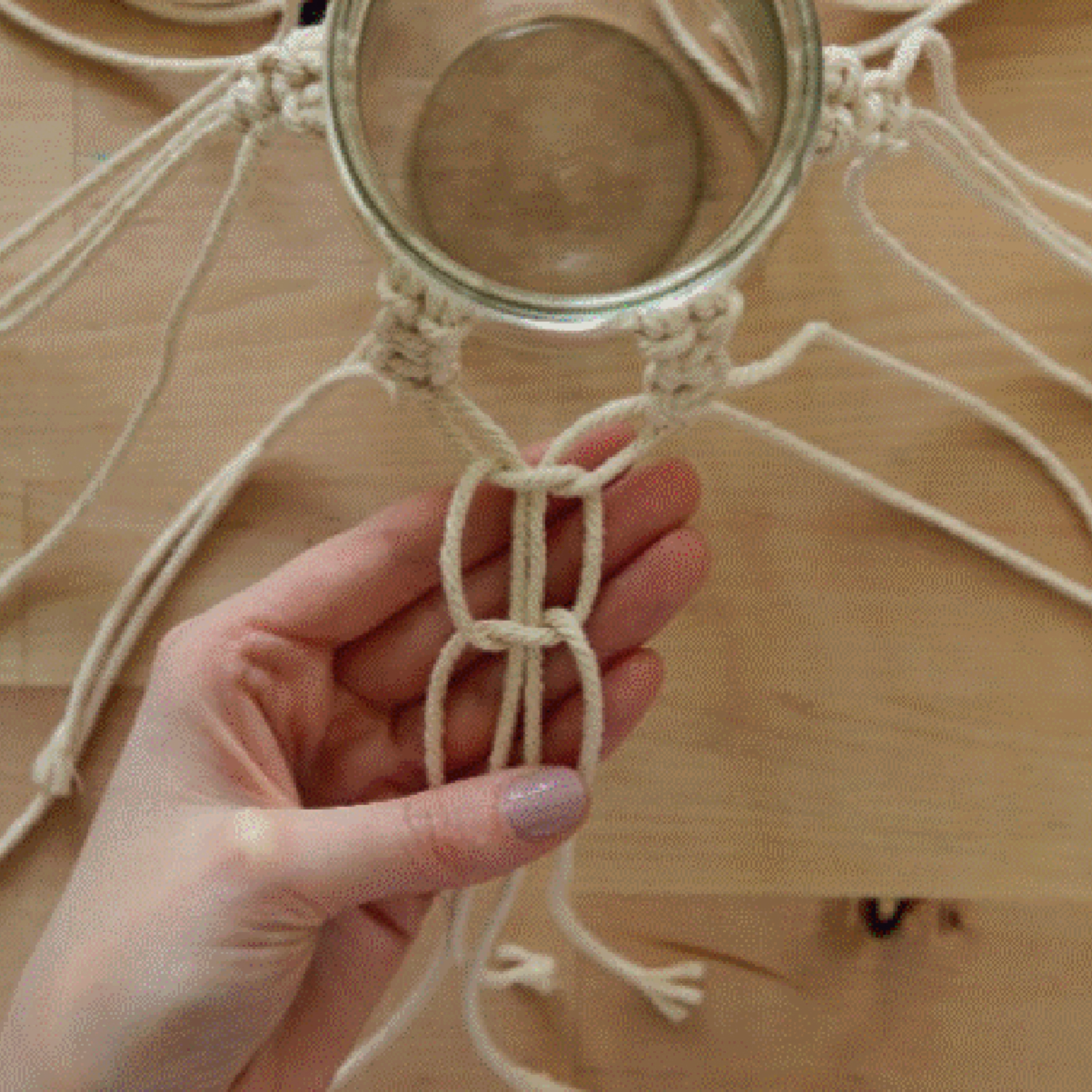 Une main noue des fils de macramé autour d'un bocal sur une table en bois.