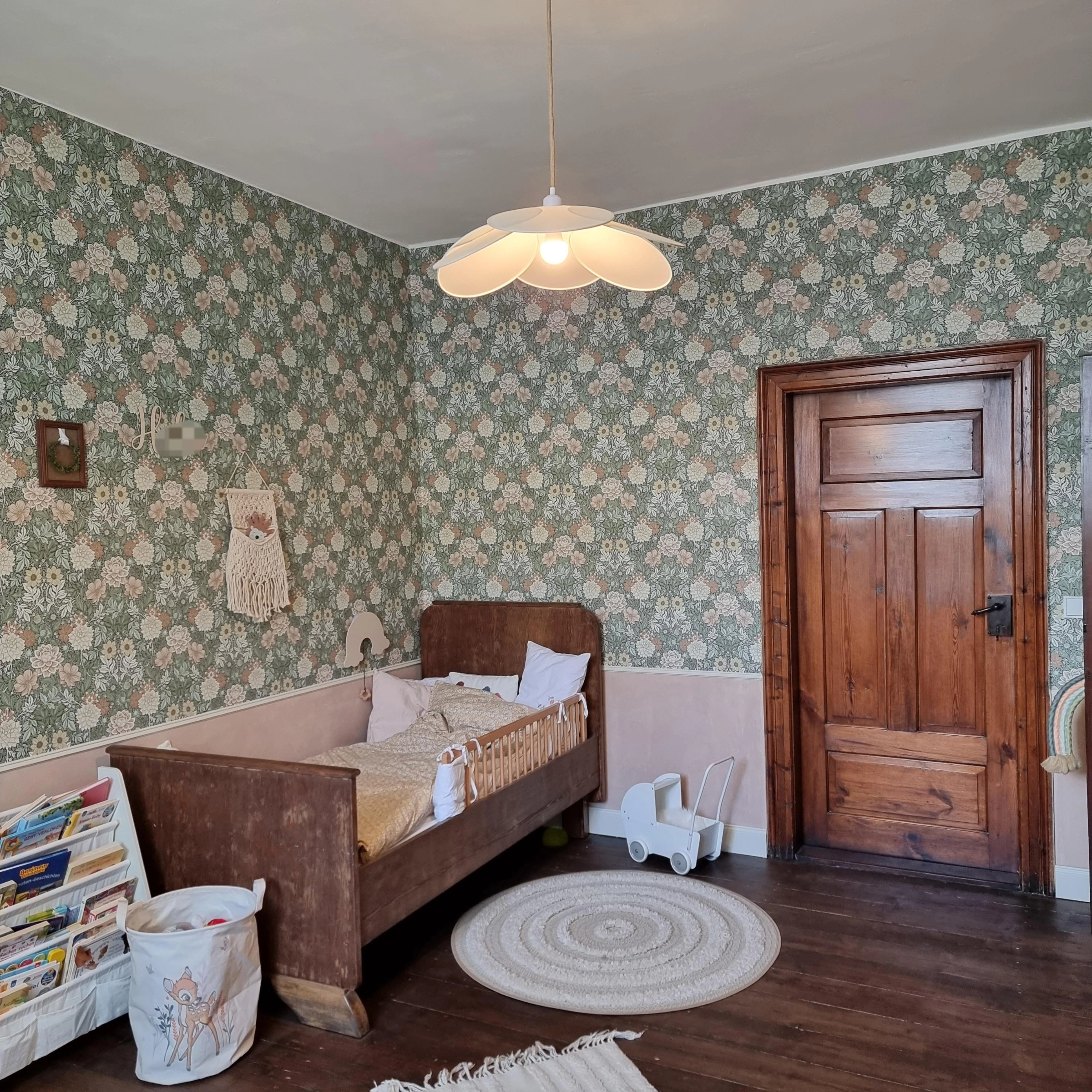 Une chambre d'enfant avec un lit en bois, du papier peint à fleurs et un tapis rond sur un sol en bois.