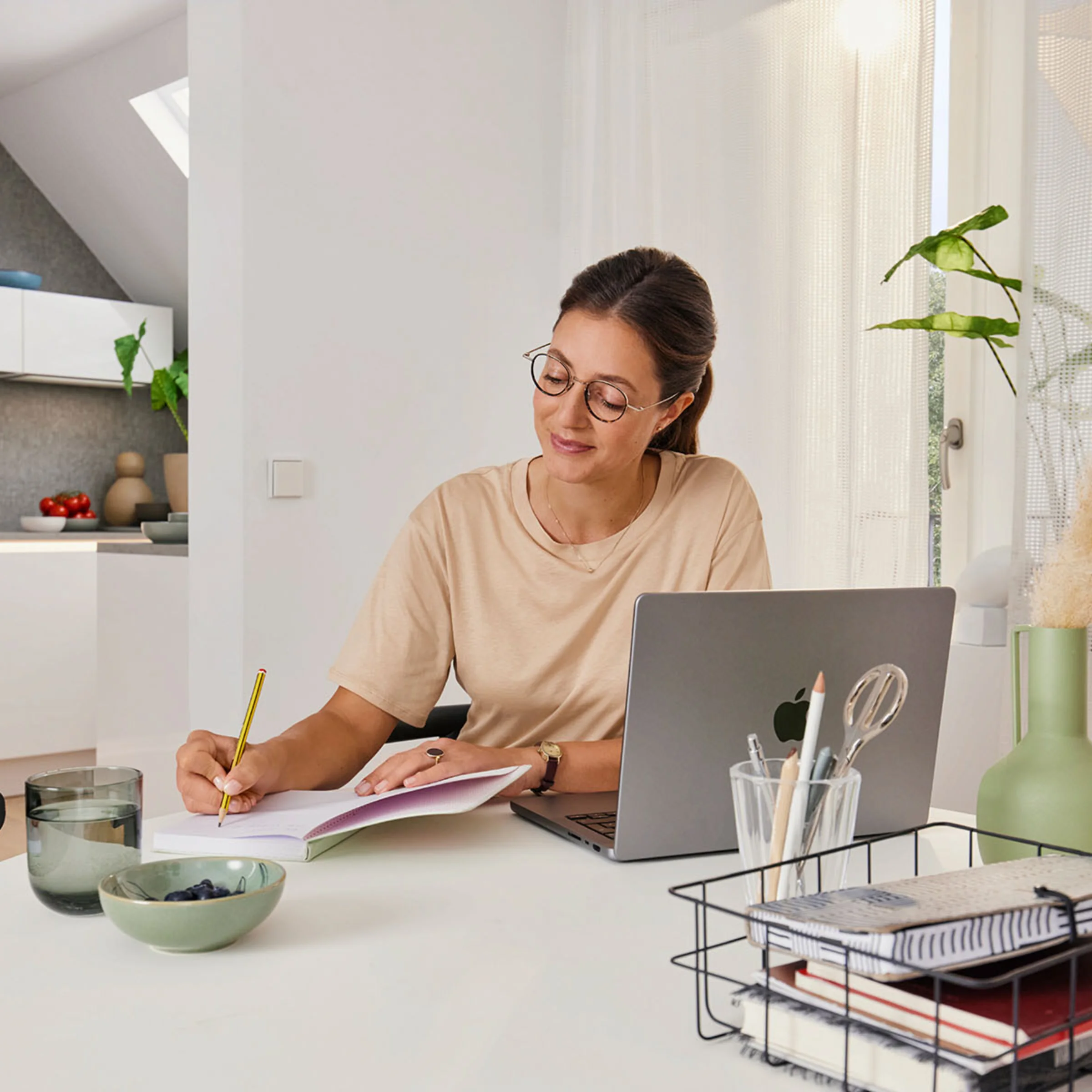 Una donna lavora a un tavolo in una stanza moderna con cucina a vista di Nolte Kitchen sullo sfondo.