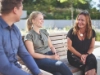 Trois personnes assises sur un banc à l'extérieur discutent par temps ensoleillé.