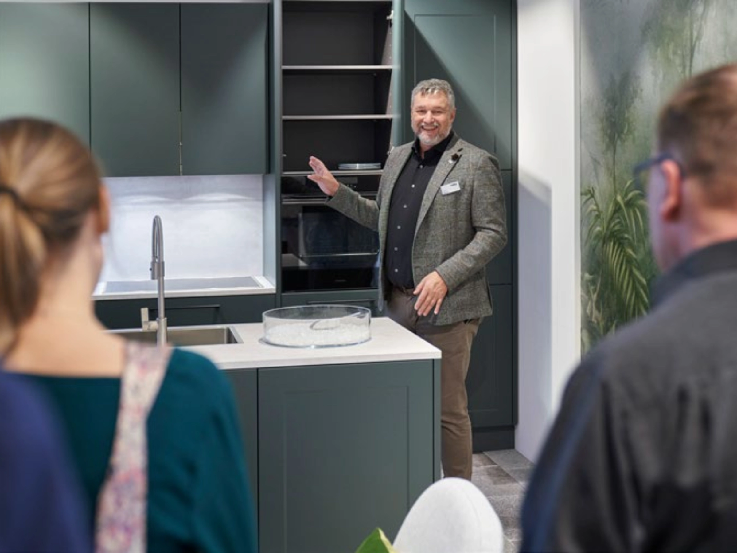 Una persona presenta una cucina moderna con armadi scuri e piano di lavoro bianco. Nolte Kitchen.