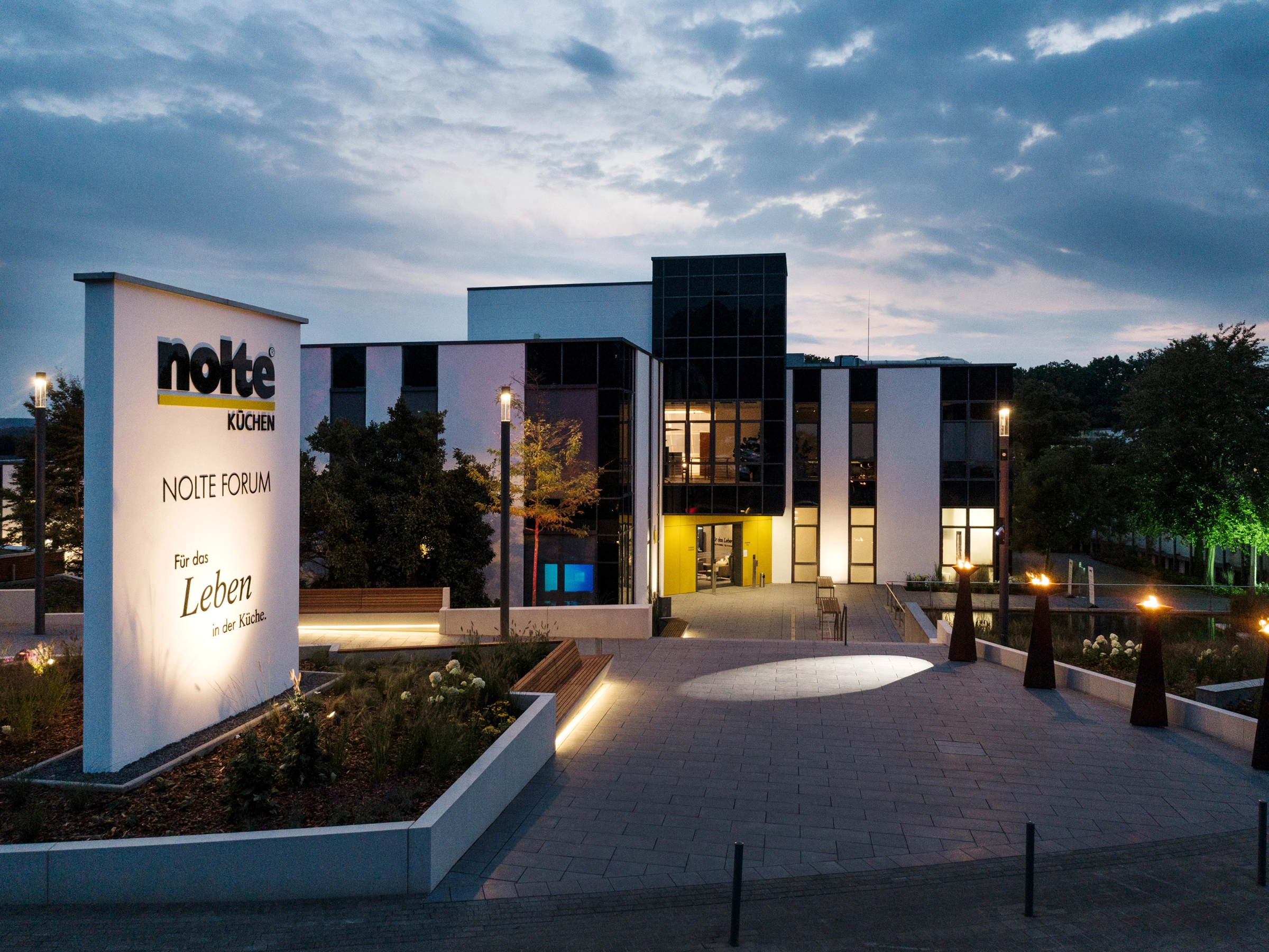The modern Nolte Forum building at dusk, surrounded by lit pathways and green spaces.
