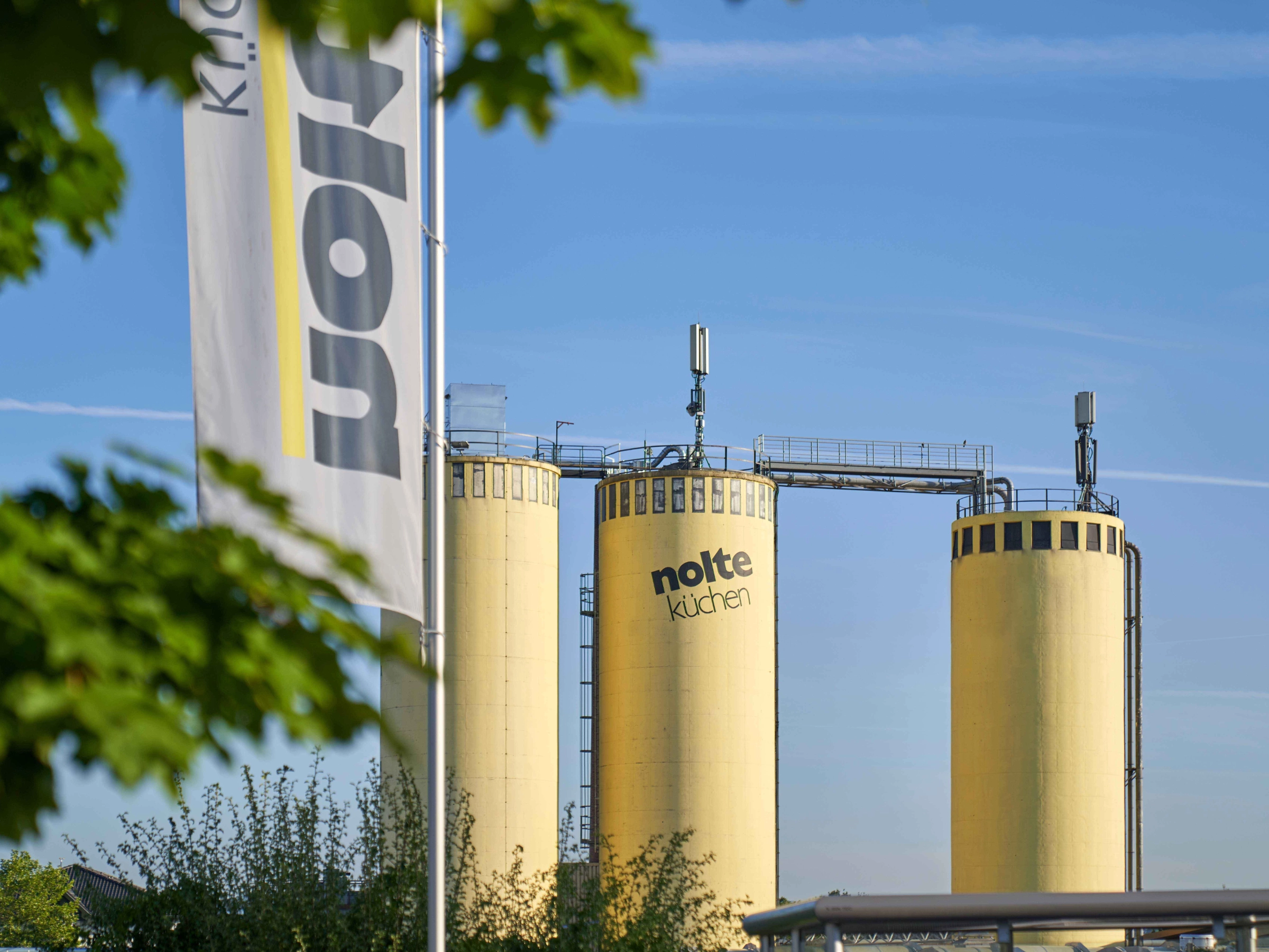 Drei gelbe Silos mit dem Logo von Nolte Küchen vor blauem Himmel.
