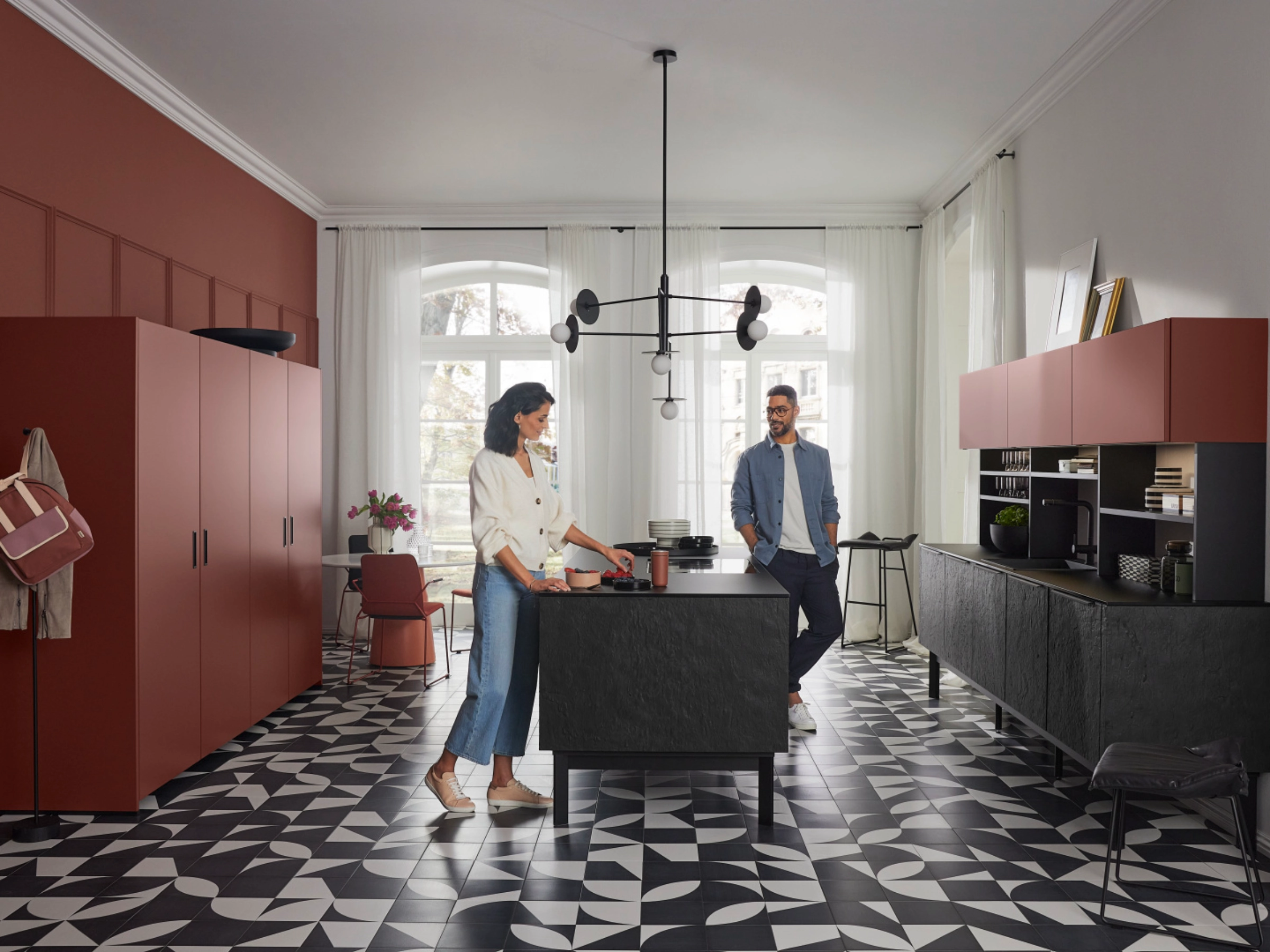 Une cuisine moderne de Nolte Kitchen avec deux personnes, sol en carreaux géométriques et armoires rouges.