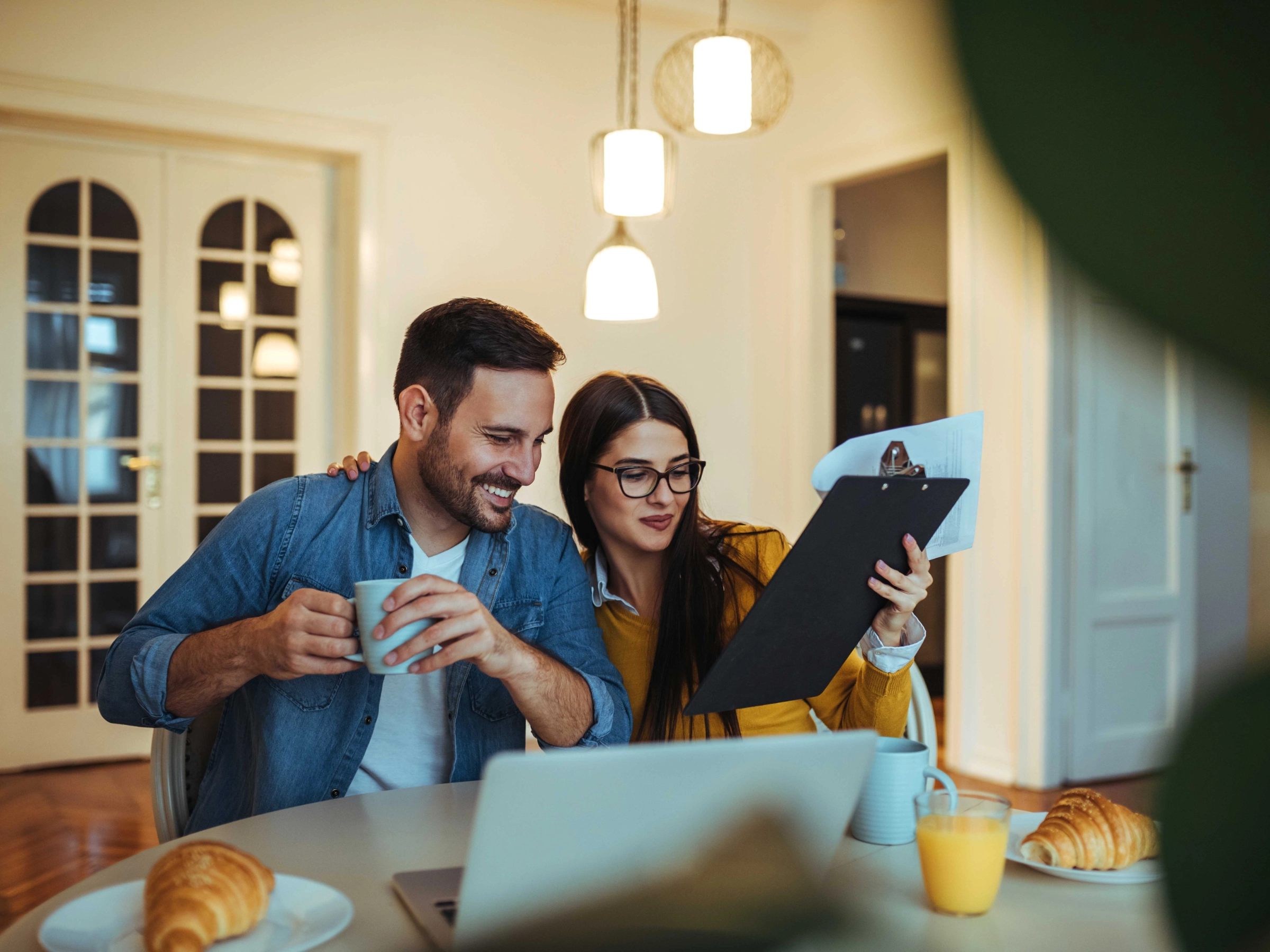Un couple est assis à table pour le petit-déjeuner avec un ordinateur portable et des documents.