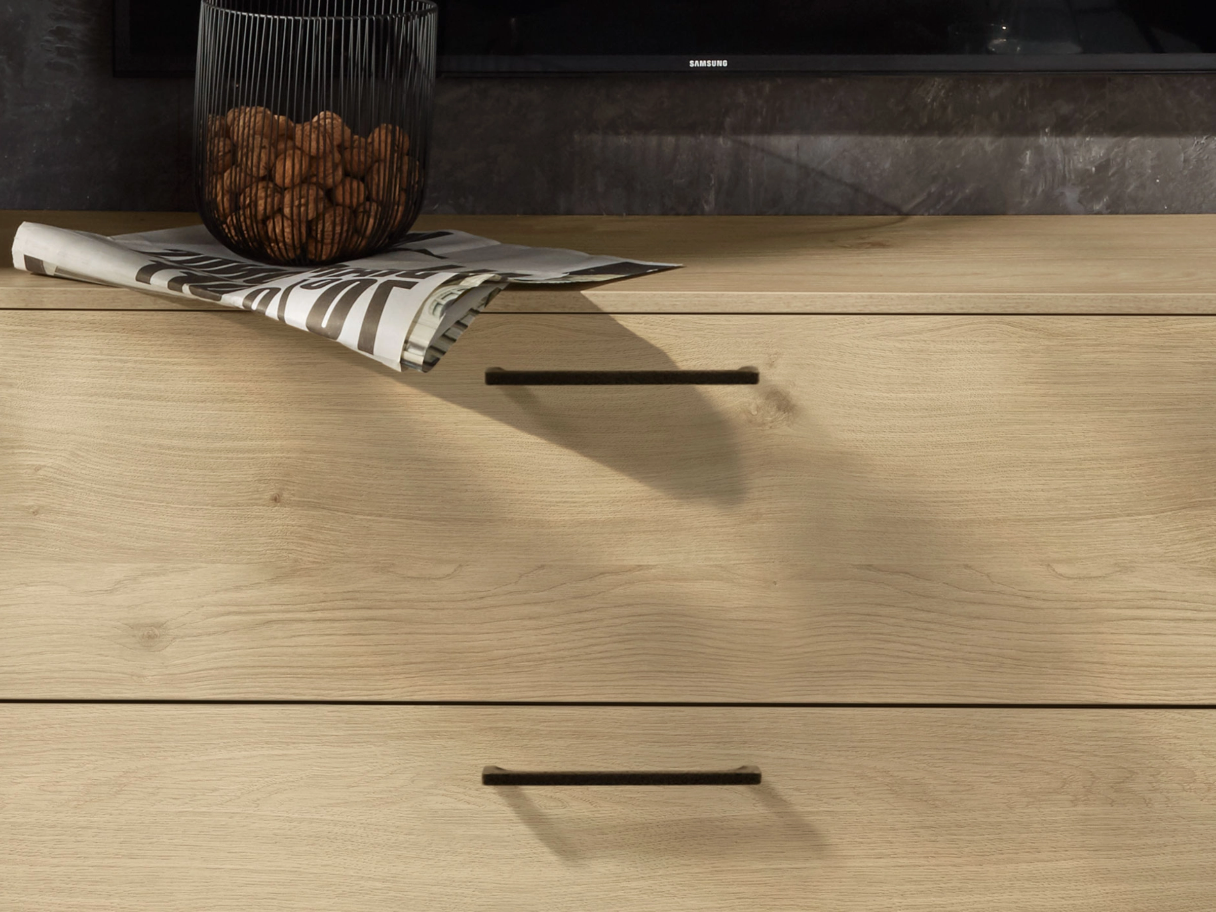 Une commode en bois clair avec décor noir et un journal dessus, assortie à Nolte Living.
