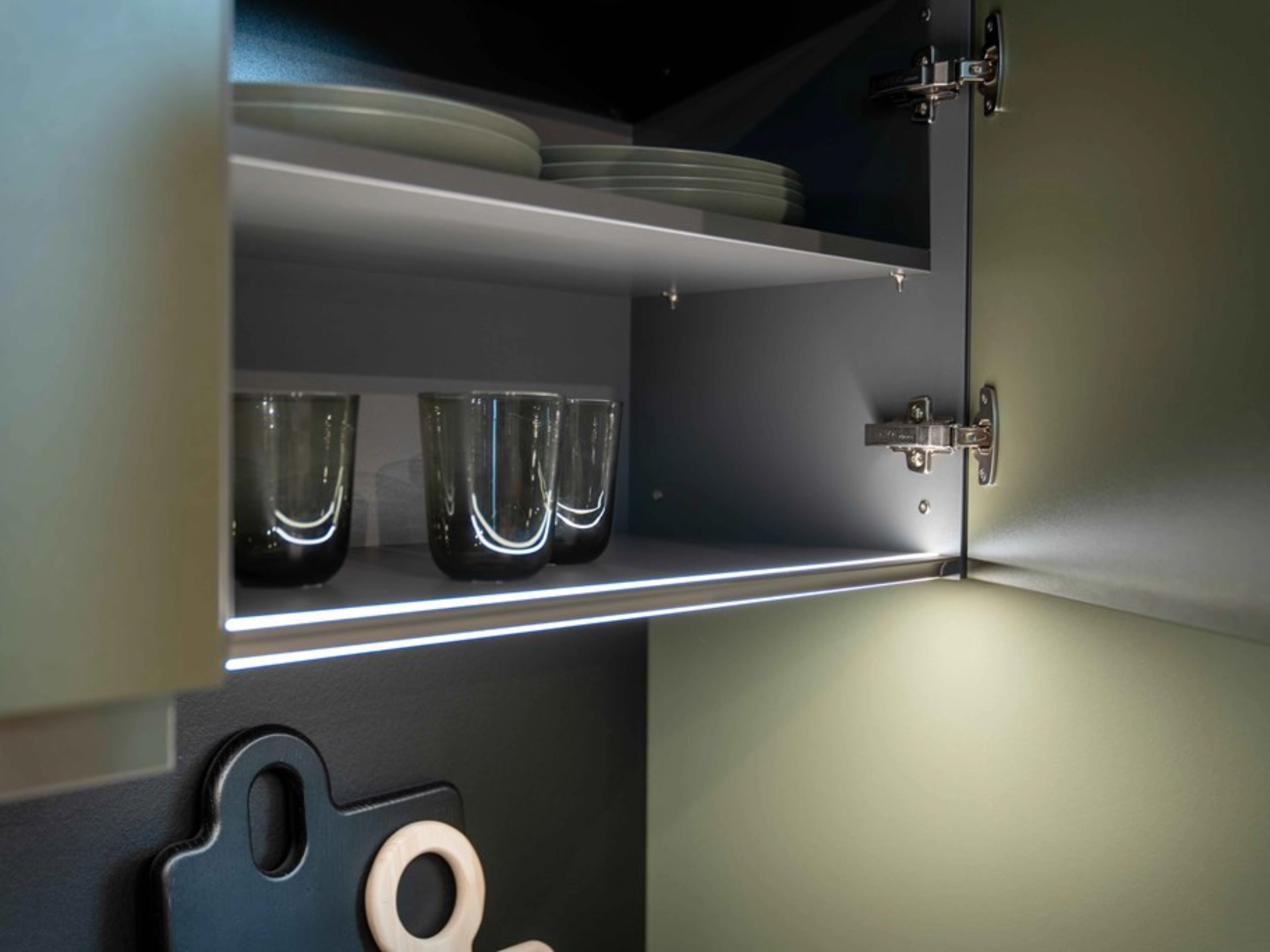Un placard de cuisine ouvert avec vaisselle et verres, éclairé de l'intérieur. Nolte Kitchen.