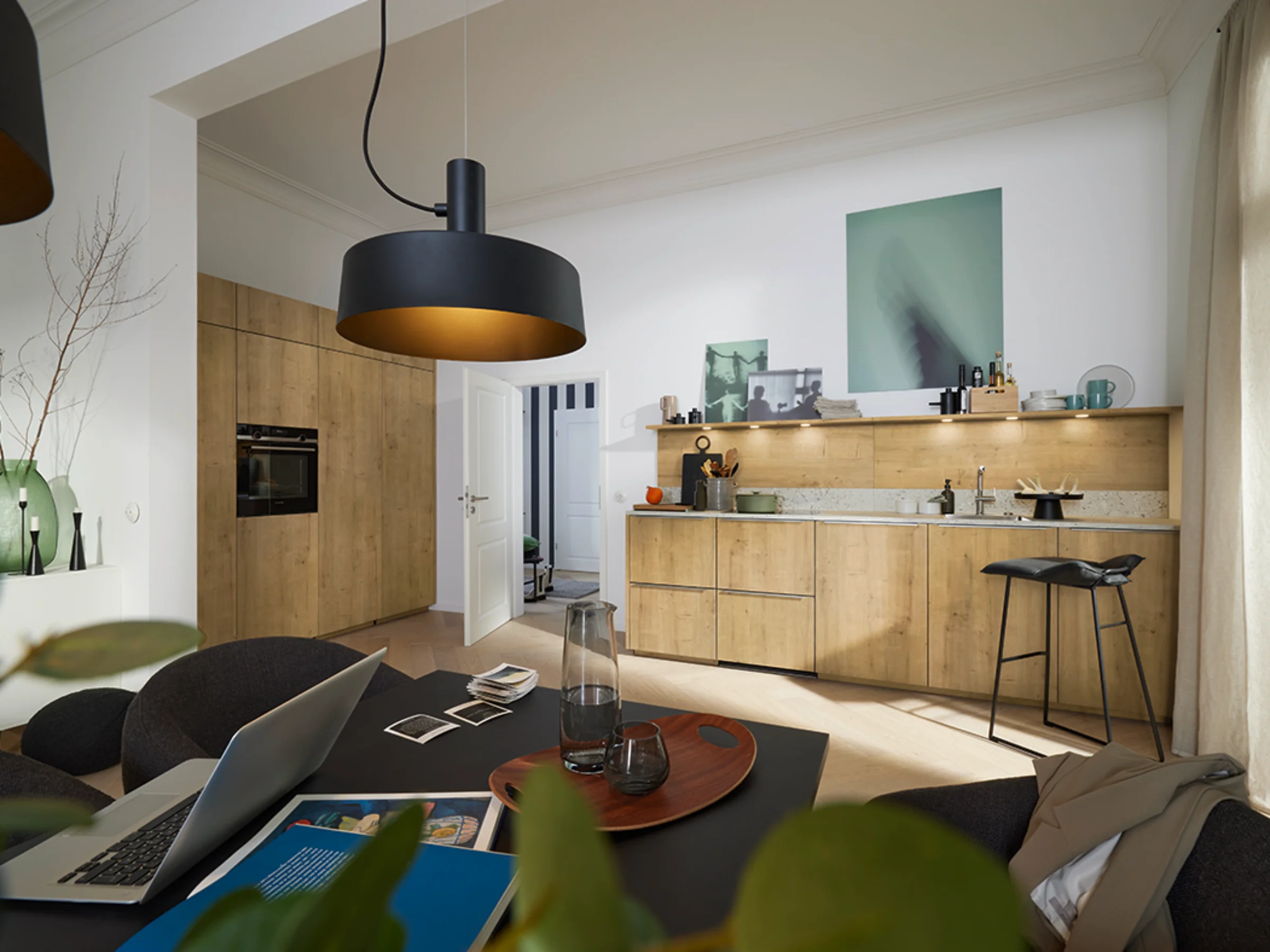 Cuisine moderne avec façades en bois et éclairage élégant, table à manger au premier plan. Nolte Kitchen.