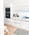 Cuisine moderne et lumineuse avec armoires blanches et tapis, élégamment conçue par Nolte Kitchen.
