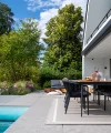 A modern garden with a terrace and pool, surrounded by trees and plants.