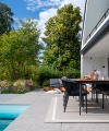 Un jardín moderno con terraza y piscina, rodeado de árboles y plantas.