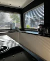 Eine moderne Küche mit weißen Schränken und großen Fenstern, die viel Licht hereinlassen. Nolte Küchen.