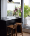 Dans une cuisine moderne avec de grandes fenêtres, deux chaises en bois sont placées contre un comptoir noir. Nolte Kitchen.