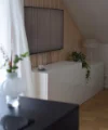 In einem modernen Wohnzimmer steht ein weißes Sideboard, dekoriert mit Pflanzen, unter einem Fernseher an der Wand. Nolte Living.
