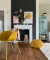 Ein stilvoll eingerichtetes Wohnzimmer mit gelbem Stuhl und Deko vor dunkler Wand; Nolte Living.