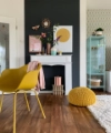 Ein stilvoll eingerichtetes Wohnzimmer mit gelbem Stuhl und Deko vor dunkler Wand; Nolte Living.