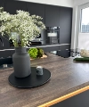 A vase with flowers sits on the countertop in a modern kitchen with dark cabinets. Nolte Kitchens.