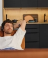 A man relaxes on a sofa in front of a modern Nolte Kitchen kitchenette.