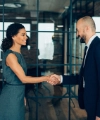 Zwei Personen in Geschäftskleidung schütteln sich die Hand in einem modernen Büro.