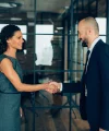 Zwei Personen in Geschäftskleidung schütteln sich die Hand in einem modernen Büro.