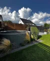 Ein moderner Garten mit Rasen, Ziergräsern und einem kleinen Pool unter blauem Himmel.
