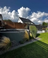 Un jardin moderne avec pelouse, graminées ornementales et une petite piscine sous un ciel bleu.