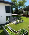 Giardino moderno con terrazza e aiuole rialzate accanto a una casa.