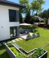 Giardino moderno con terrazza e aiuole rialzate accanto a una casa.