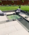 Giardino moderno con vasca d'acqua e area salotto, circondato da prato curato e piante.