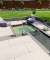 Giardino moderno con vasca d'acqua e area salotto, circondato da prato curato e piante.