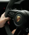 Une personne tient le volant d'une voiture avec un logo Porsche.