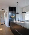 Cocina moderna con isla oscura y lámparas colgantes, refrigerador al fondo. Nolte Cocina.