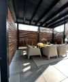Eine überdachte Terrasse mit Tisch und vier Stühlen aus Rattan, umgeben von Holzlamellenwänden.