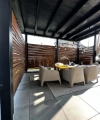 Une terrasse couverte avec une table et quatre chaises en rotin, entourée de murs à lames de bois.