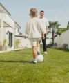 Un enfant joue au football avec un adulte dans le jardin.