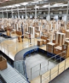 In einer großen Lagerhalle stehen zahlreiche verpackte Holzteile auf Förderbändern.