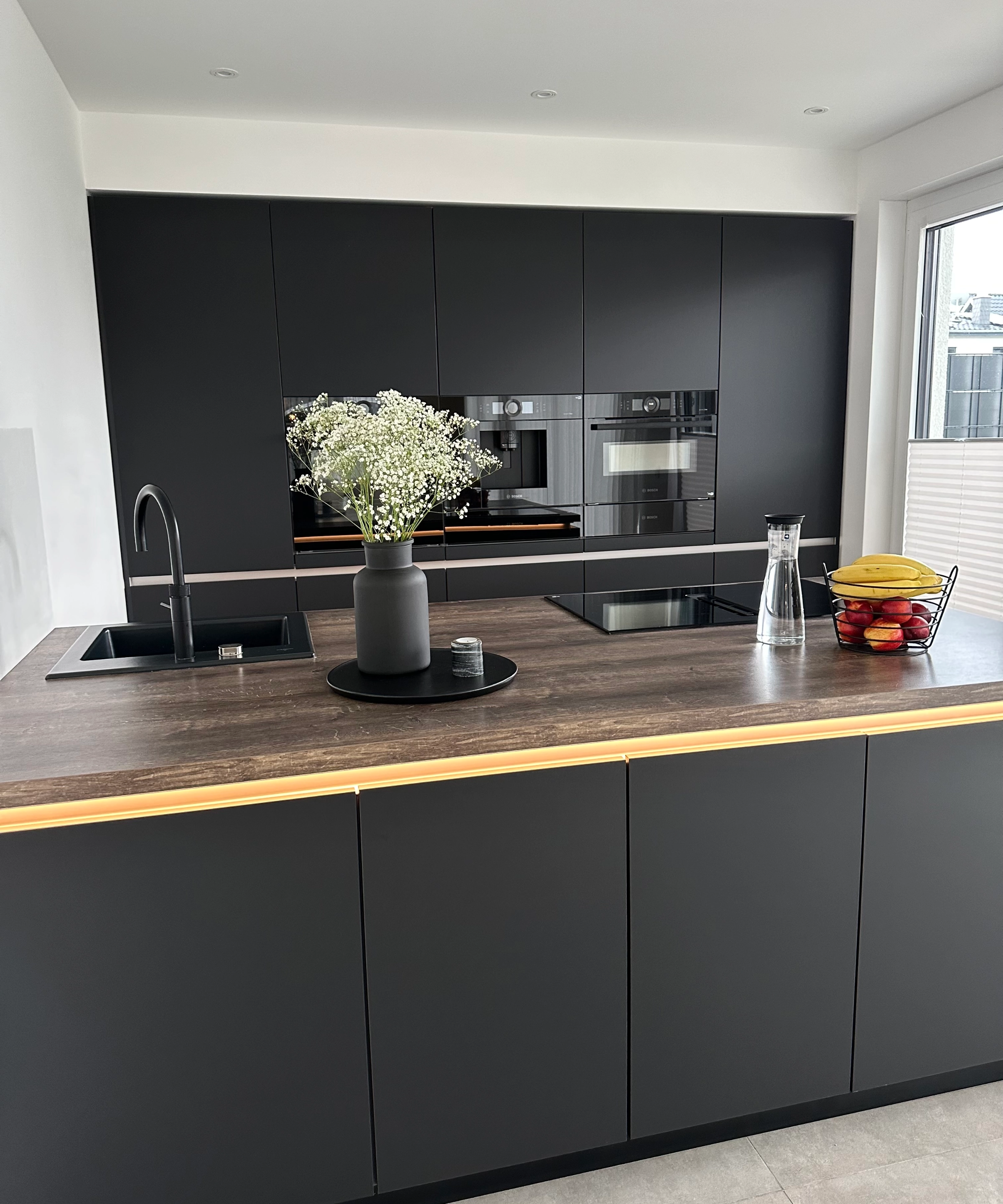 A modern kitchen with dark cabinets and an island, decorated with flowers, by Nolte Kitchen.