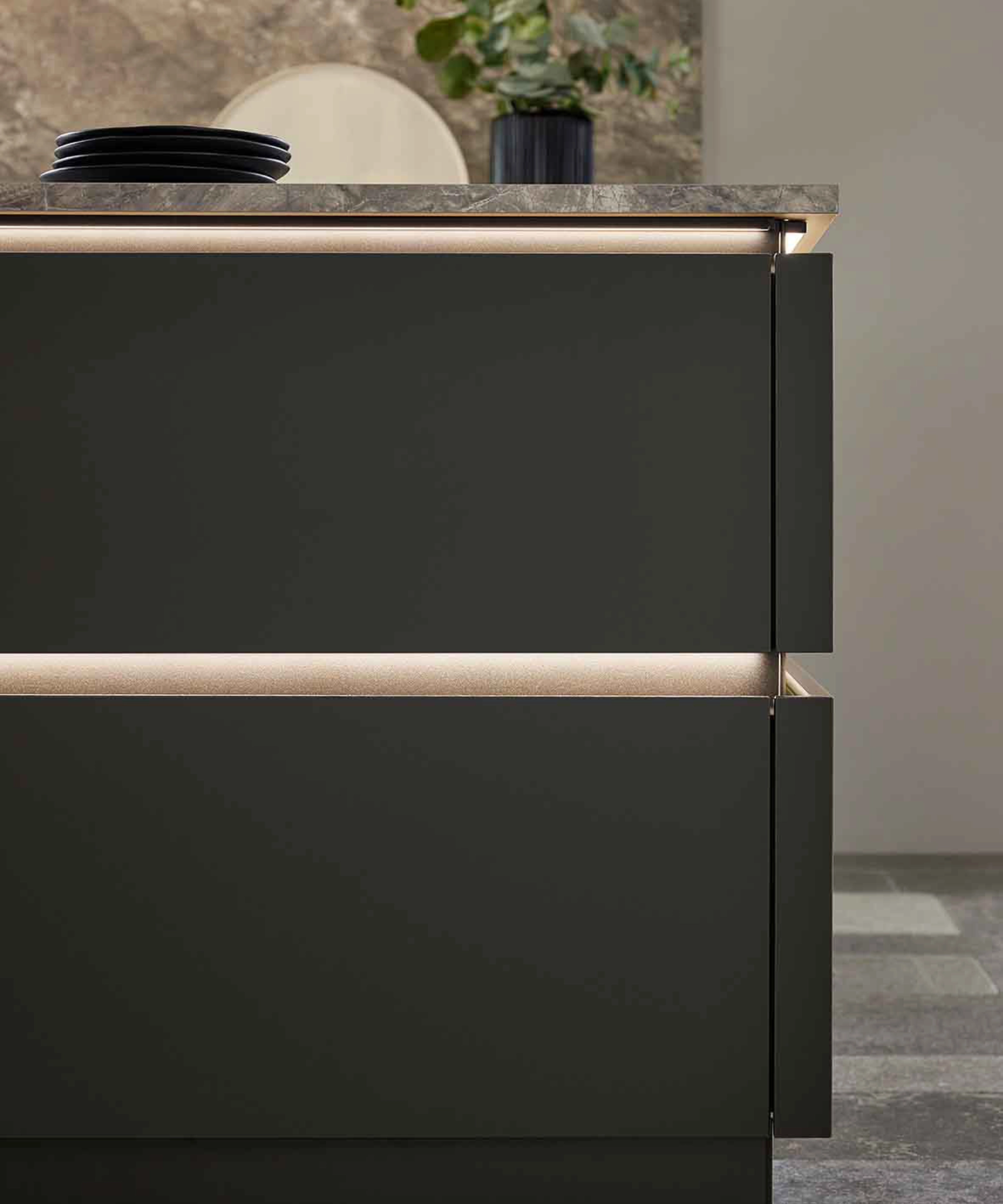 Eine moderne Küchenschublade mit eleganter Beleuchtung, im Hintergrund dekorative Pflanzen. Nolte Küchen.