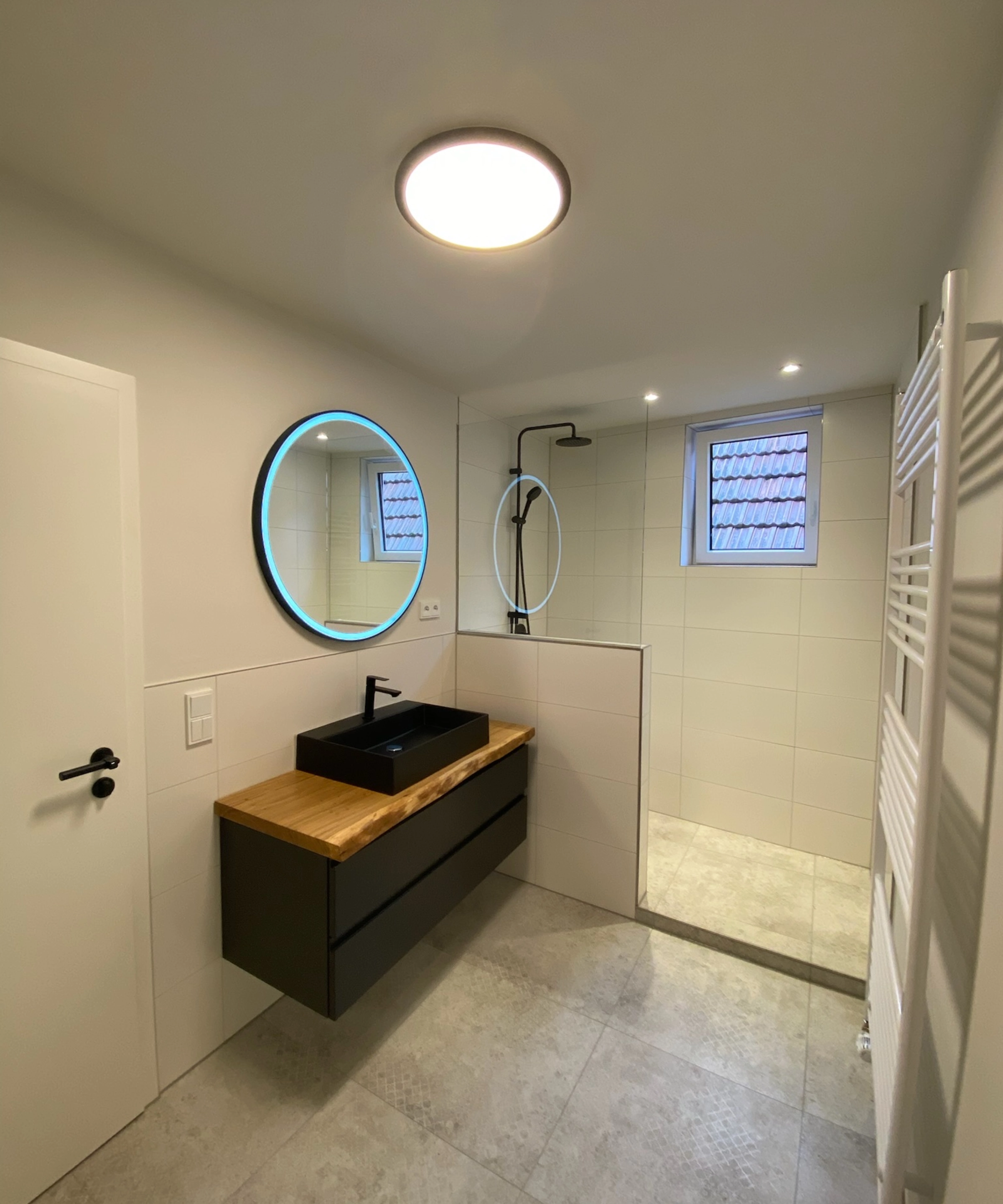 Salle de bain moderne avec lavabo noir et miroir rond éclairé, Nolte SPA.