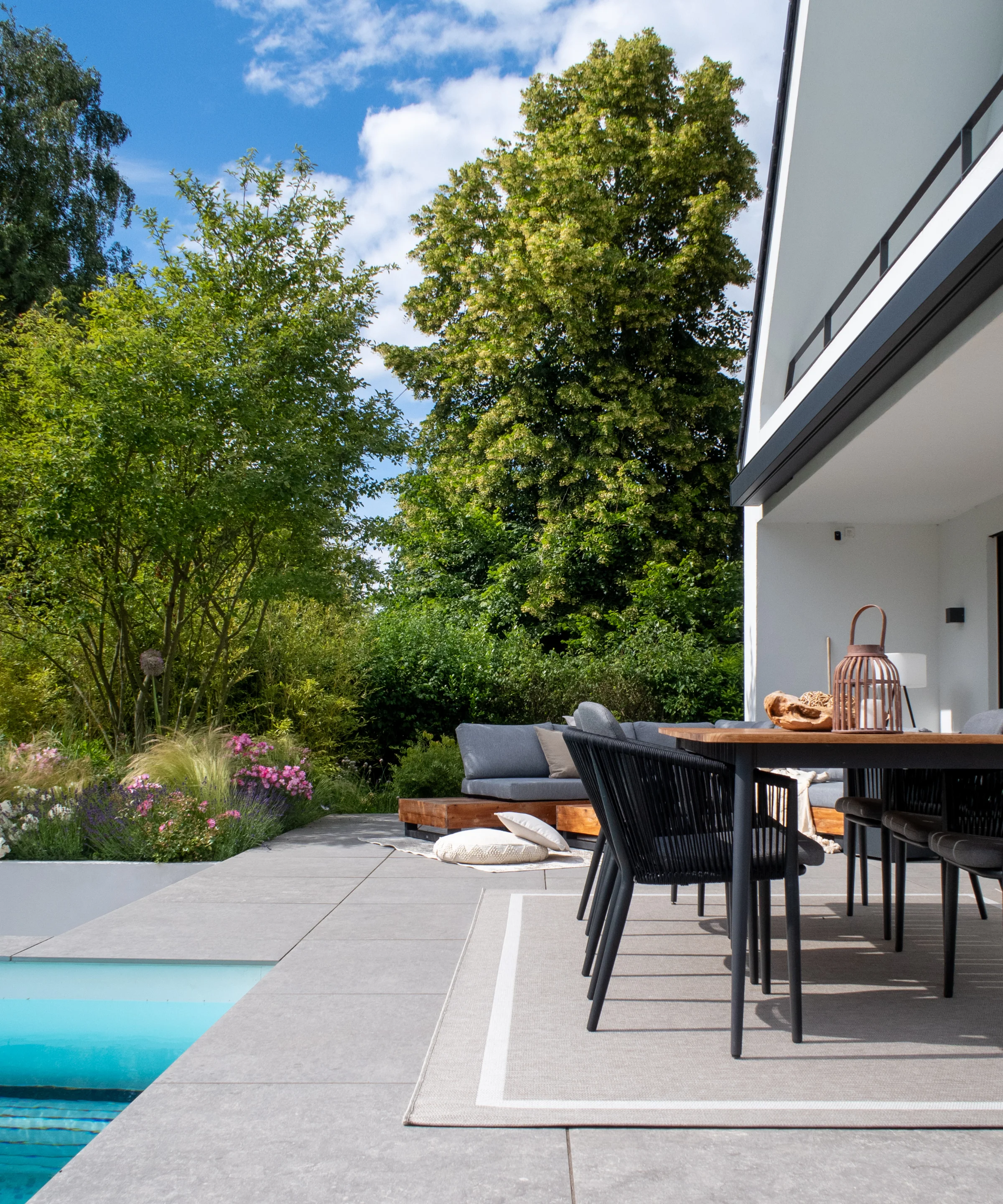 A modern garden with a terrace and pool, surrounded by trees and plants.