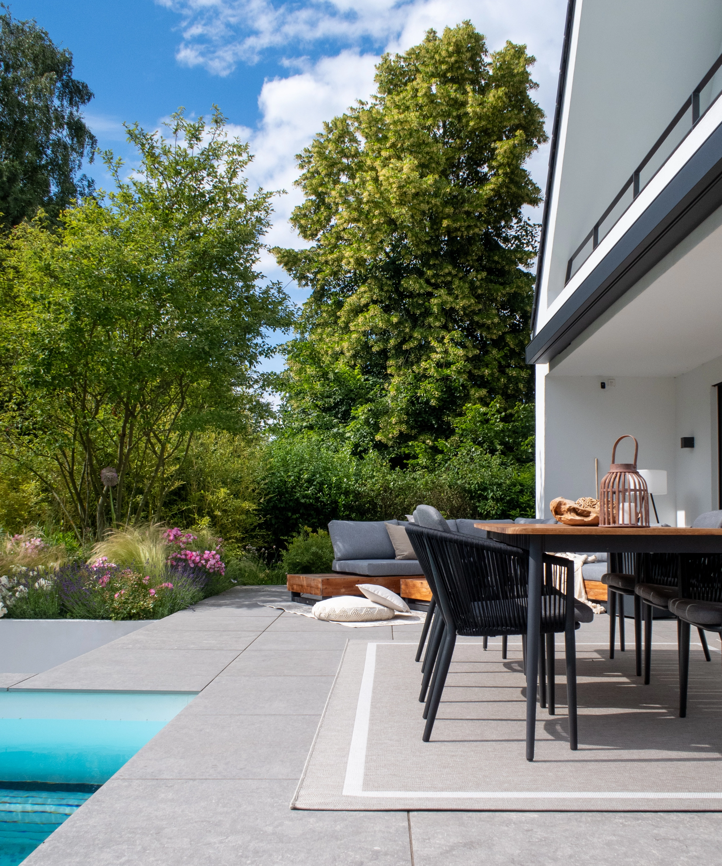 Un jardín moderno con terraza y piscina, rodeado de árboles y plantas.