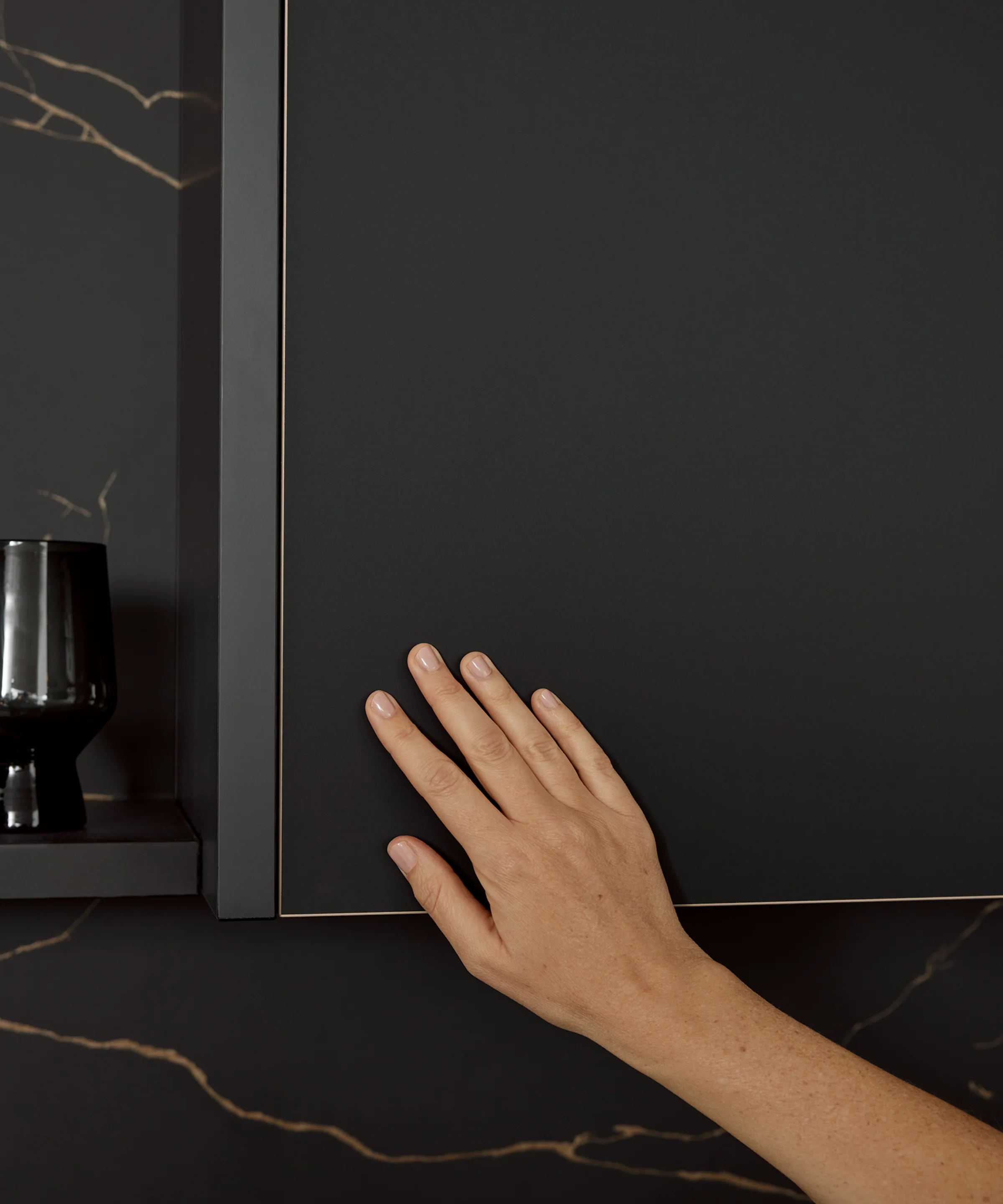 Een hand raakt een elegante zwarte keukenkast aan. Nolte Küchen.