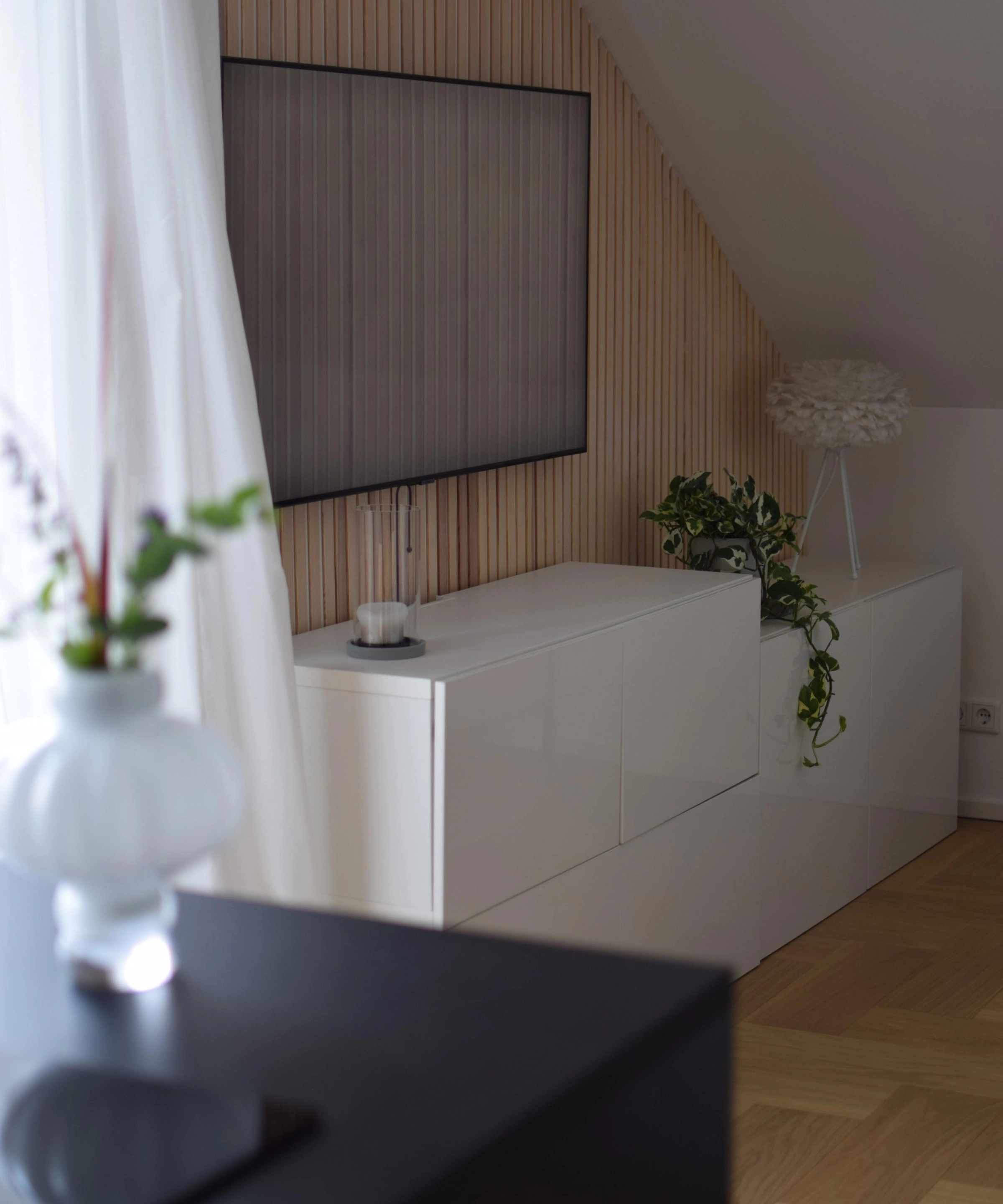 Dans un salon moderne, un buffet blanc décoré de plantes se trouve sous une télévision murale. Nolte Living.