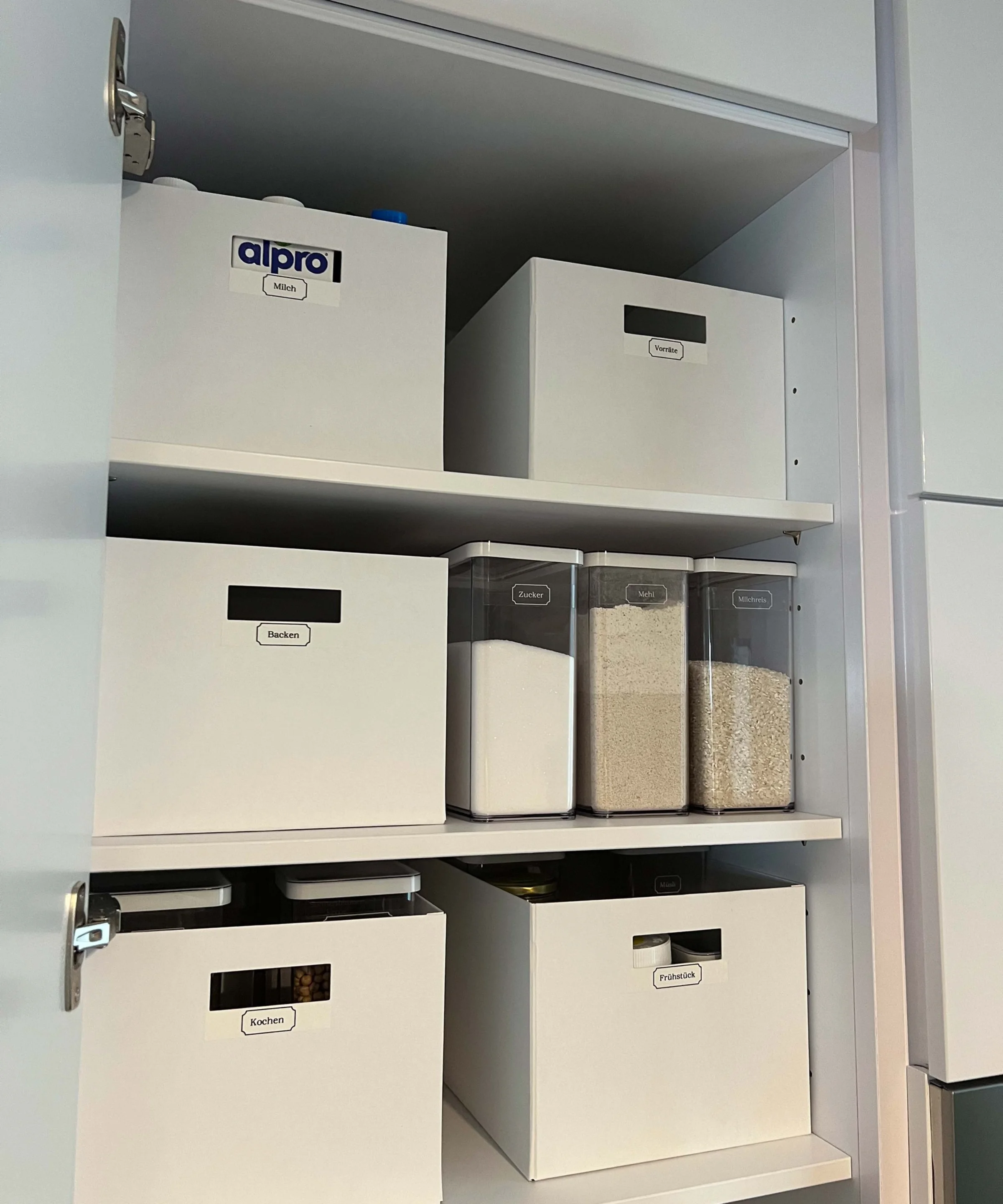 Ein geöffneter Schrank mit beschrifteten Vorratsboxen und -gläsern in einem Nolte Hauswirtschaftsraum.