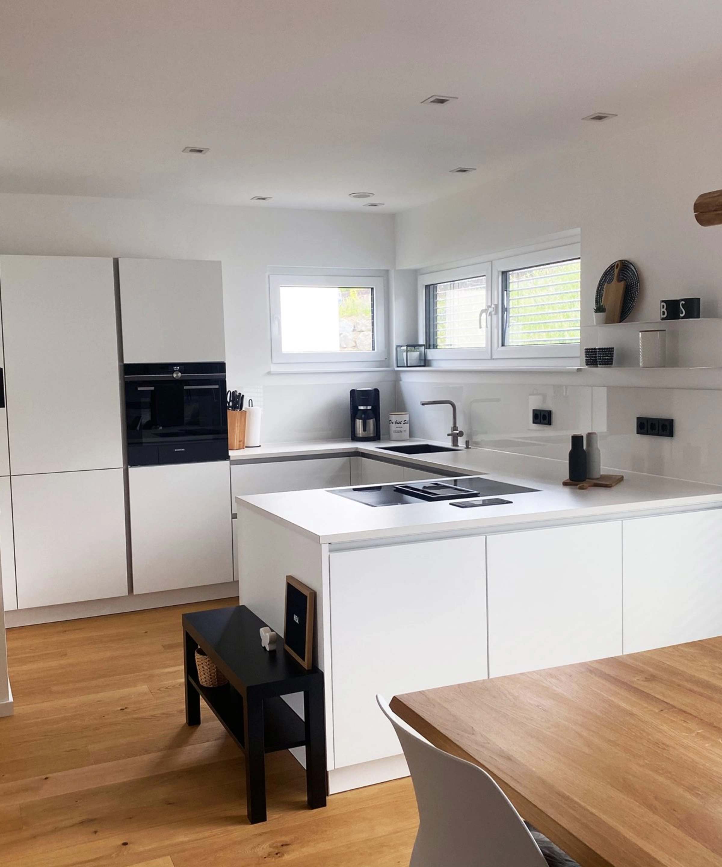 Une cuisine moderne blanche avec des détails en bois et un îlot, équipée par Nolte Kitchen.