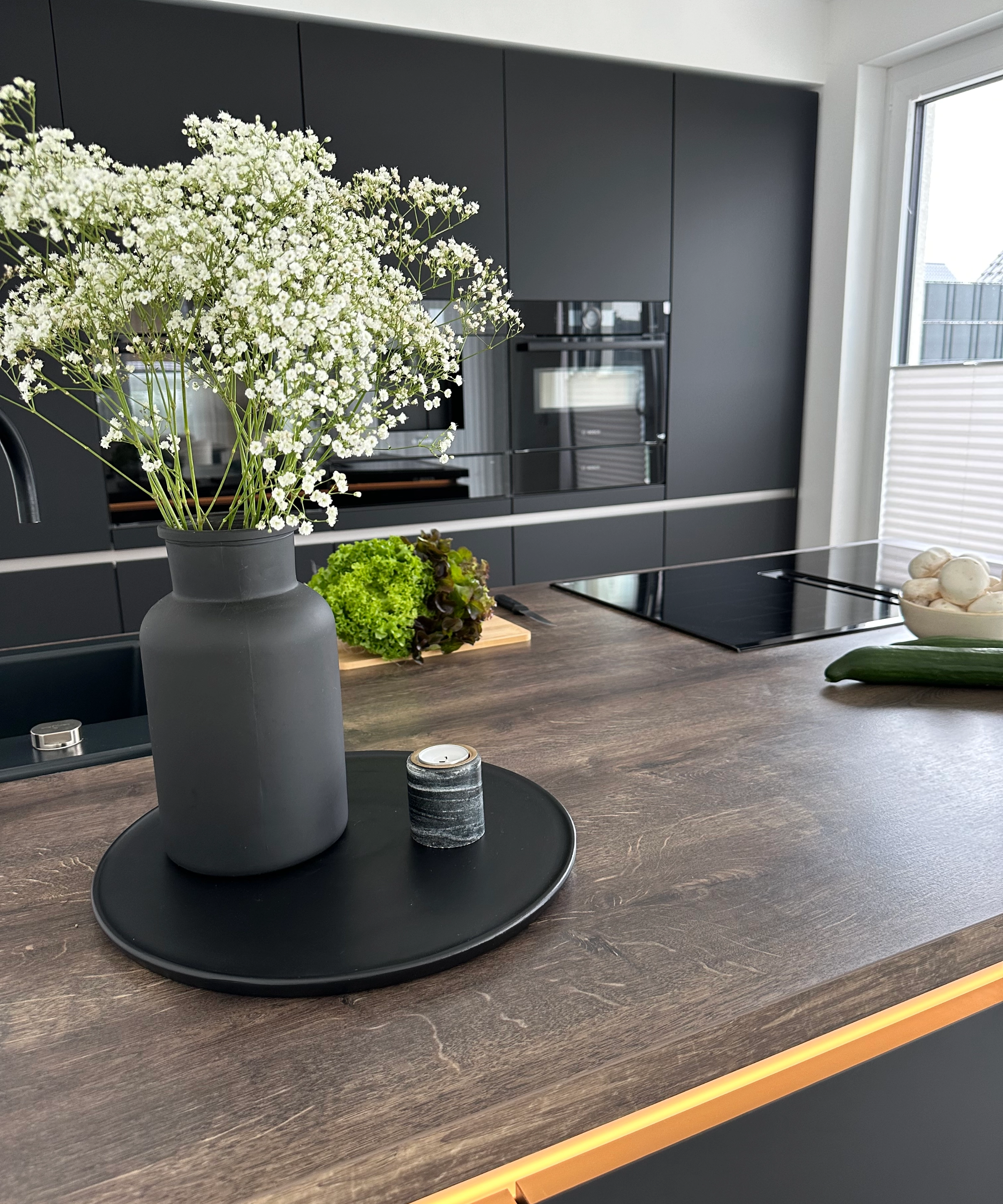 A vase with flowers sits on the countertop in a modern kitchen with dark cabinets. Nolte Kitchens.
