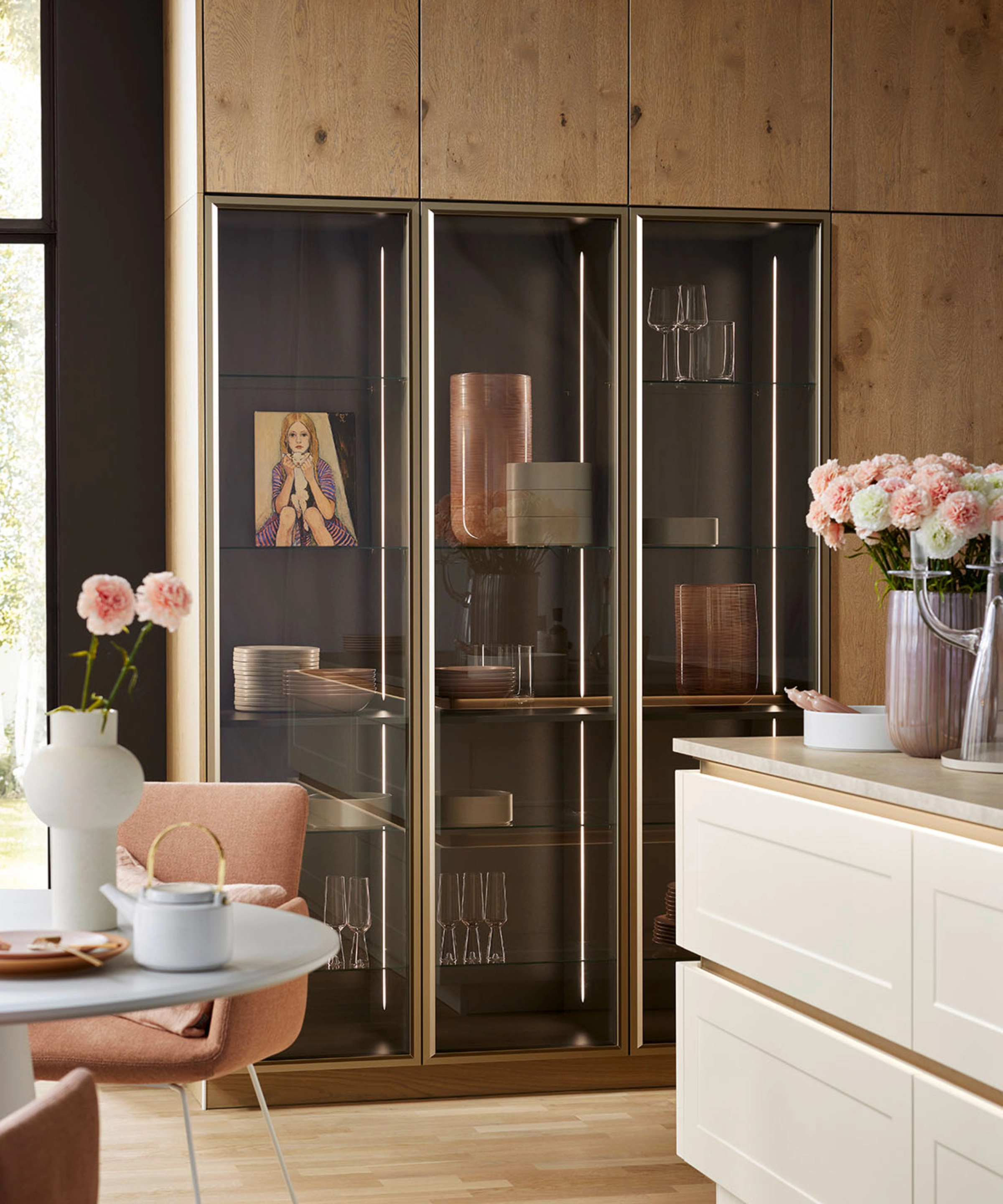Eine moderne Küche mit Holz- und Glaselementen, dekoriert mit Blumen, zeigt das Design von Nolte Küchen.