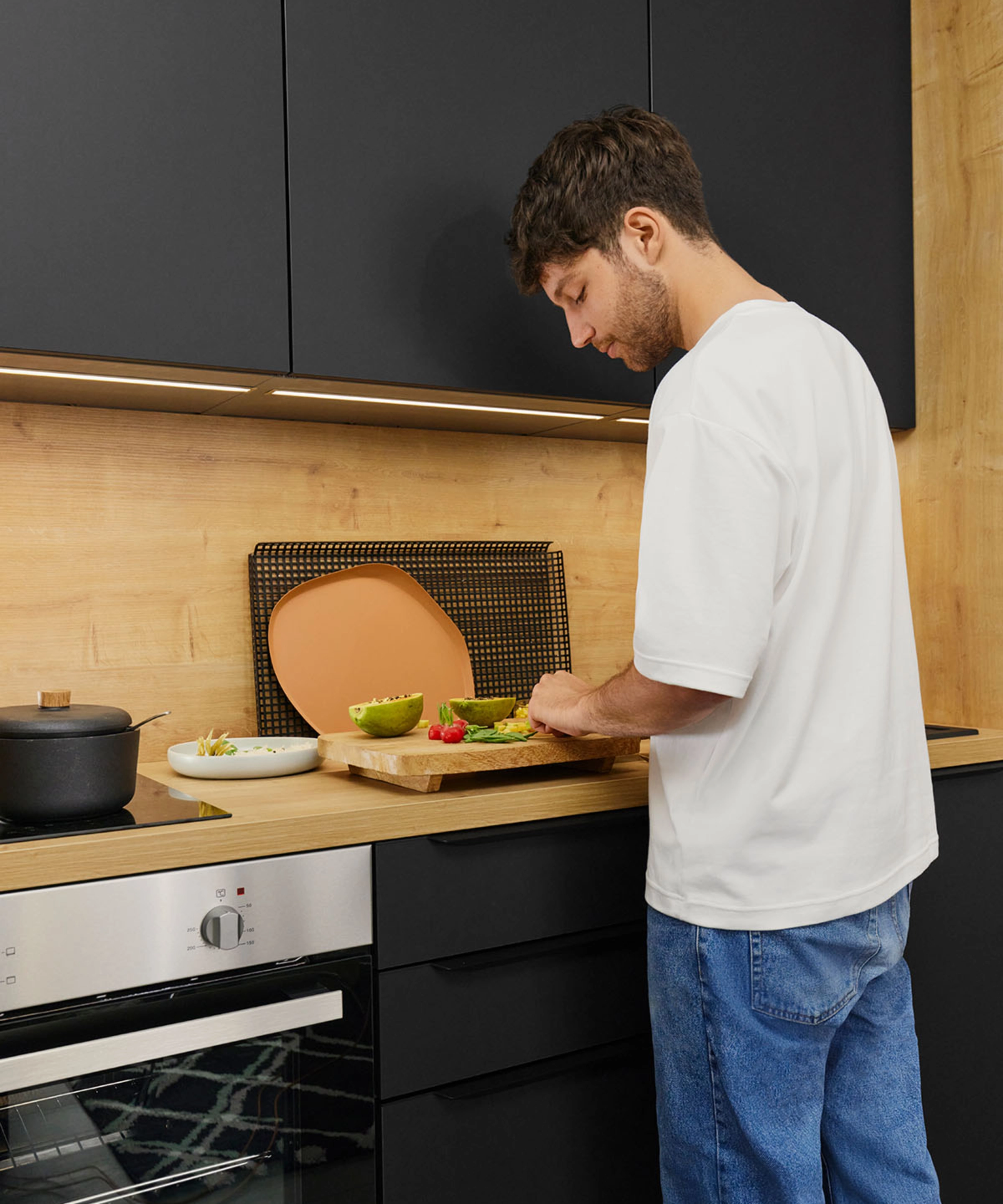 A man chopping vegetables in a modern kitchen with black cabinets. Nolte Kitchen.